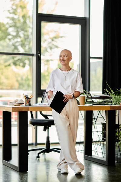 A young bald woman stands gracefully in an office, showcasing her elegant outfit and vibrant smile.
