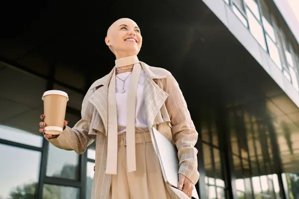 stock image A bald woman dressed elegantly stands outside, holding a coffee cup and smiling brightly.