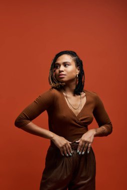 Saçları örgülü, şık, genç bir Afro-Amerikan kadın stüdyoda duruyor ve eşsiz tarzını sergiliyor..