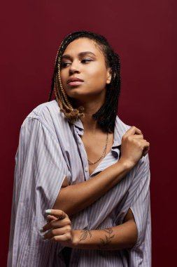 Saçları örgülü şık, genç bir Afrikalı Amerikalı kadın dikkat çekici bir stüdyo resminde tarzını sergiliyor..