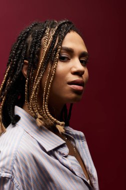 Saçları örgülü, zarif genç bir kadın, eşsiz tarzını sergileyerek zengin bir arkaplanda poz veriyor..