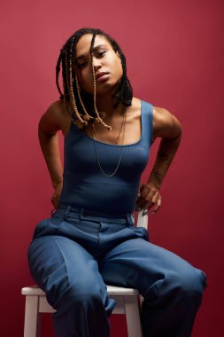 Genç bir kadın saç örgüsü ve canlı bir arka planda kendine güvenen bir bakışla stüdyoda tarzını sergiliyor..