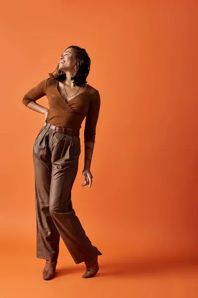 stock image A stylish African American woman with braids poses confidently against a vibrant orange background.