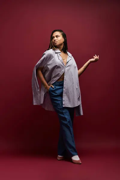 stock image A young African American woman poses confidently in a stylish outfit against a rich backdrop, exuding elegance.