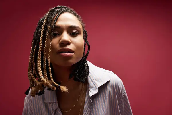 stock image An elegant young woman showcases her braided hairstyle in a creative studio against a bold backdrop.