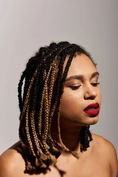 stock image A young woman showcases her unique braided hairstyle and bold red lips in a modern studio environment.