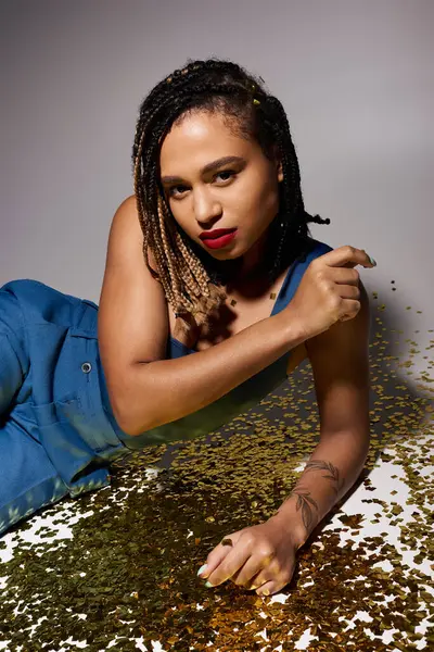 stock image A chic young woman with braided hair and vibrant red lips showcases her unique style against a shimmering backdrop.