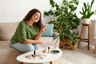 Kıvırcık saçlı bir kadın oturma odasında dinleniyor. Güzellik ürünleriyle mutlu mesut meşgul olurken hazırlanıyor..