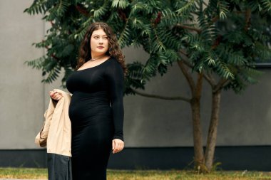 Siyah elbiseli ve trençkotlu kendinden emin, iri yarı bir kadın sonbahar havasını canlı yapraklar arasında kucaklıyor..