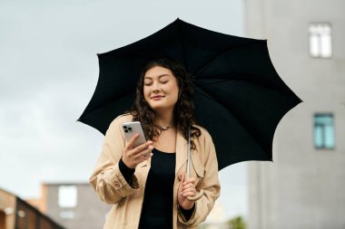 Sonbahar havasının ortasında, siyah elbiseli ve trençkotlu genç bir kadın telefonunu kontrol ediyor..