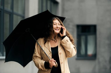 Genç, iri yarı bir kadın sıcak ve neşe saçan bir sonbahar gününde şemsiyesini tutarken gülümser..