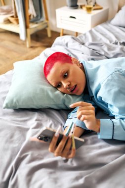 Genç bir kadın evinde akıllı telefonuyla derinden meşgul bir şekilde bir yatakta rahatça uzanır..