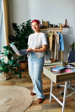 A young woman with vibrant pink hair engages with her laptop in a stylish, plant filled room. clipart