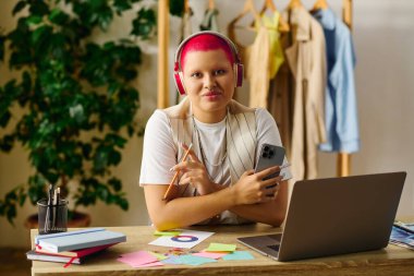 A young woman with bright pink hair works on creative projects while enjoying her home environment. clipart