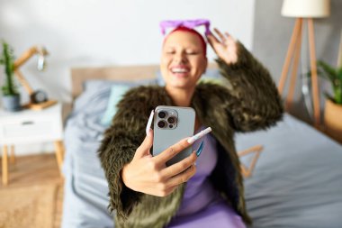 Neşeli genç bir kadın, hareketli ruhunu yansıtan modaya uygun yatak odasında selfie çekiyor..