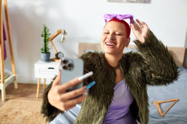 Genç bir kadın neşeyle selfie çeker. Parlak, rahat bir odada vakit geçirir..