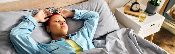 A young woman lies in bed, her fingers stretching behind her head while she contemplates her day.