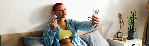 A young woman enjoys a carefree moment taking a selfie in her stylish bedroom setting.