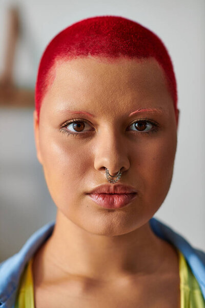 Уверенная в себе молодая женщина с ярко-рыжими волосами представляет свой смелый взгляд в уютной домашней обстановке.