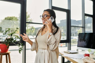 Genç bir kadın modern ofis ortamında dururken telefonuyla iletişim kuruyor..