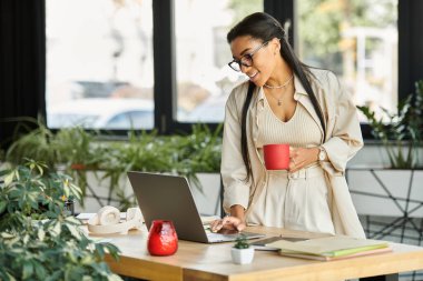 A cheerful woman collaborates on her laptop, sipping coffee in a vibrant, plant filled workspace. clipart