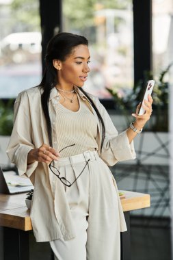 A young, attractive woman in an office checks her smartphone with a stylish, confident demeanor. clipart