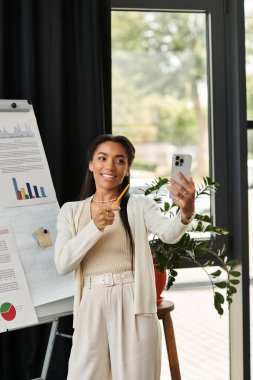 Genç ve güzel bir kadın neşeli bir ofiste bitkilerle süslenmiş bir selfie çekiyor..