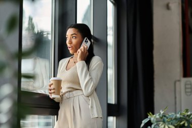 Genç ve güzel bir kadın büyük bir pencerenin yanında duruyor, canlı bir telefon görüşmesi yapıyor..