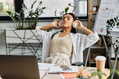 A young woman leans back in her chair, headphones on, savoring a moment of calm amid office tasks. clipart