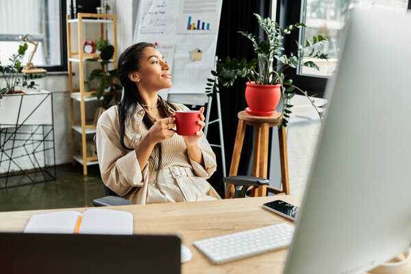 A young woman sits comfortably in her office, savoring a warm cup of coffee and contemplating.