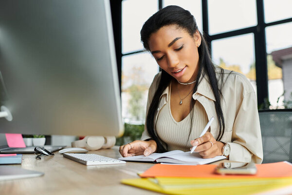 A beautiful young woman is focused on jotting down notes at her sleek office desk in daylight.