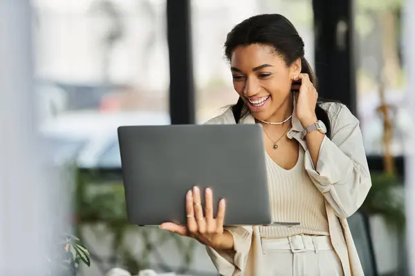 stock image A young woman smiles while interacting online from her stylish office, showcasing enthusiasm.