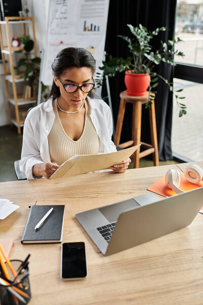Уверенная в себе женщина рассматривает документы на своем рабочем месте, заполненном зеленью и мягким светом.
