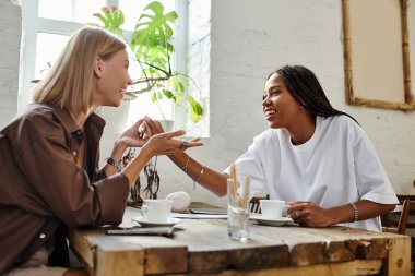 A happy multicultural couple enjoys each others company while sharing coffee in a chic cafe setting. clipart