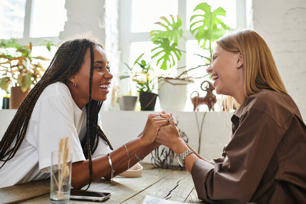 Радостный момент разворачивается, когда две женщины держатся за руки и глубоко улыбаются друг другу в очаровательном кафе.