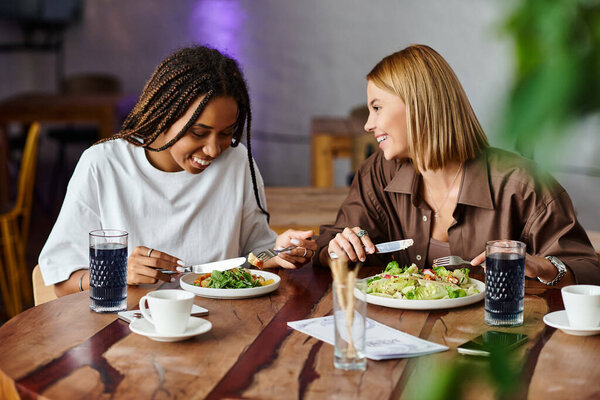 Улыбающаяся афроамериканка делит восхитительный обед со своей девушкой в очаровательном кафе.