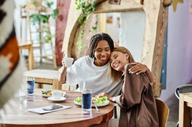 A smiling African American woman enjoys a charming moment with her girlfriend at a cafe, savoring lunch together. clipart