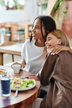 A happy multicultural couple shares a tender moment at a cafe, savoring tasty dishes and each others company. clipart