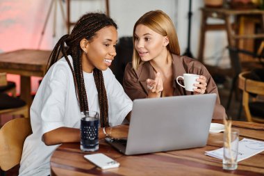 Sıcak bir kafe atmosferi, çok ırklı bir çiftin birlikte çalışırken kahkaha ve sevgisini paylaştığını vurguluyor..
