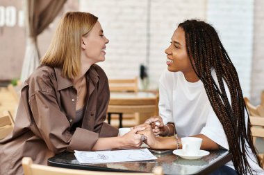 Neşeli, çoklu etnik çeşitlilikte bir çift, bir kafede gülümseyerek ve özel bir anı paylaşarak birbirlerine eşlik etmekten zevk alır.