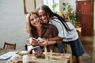 A joyful African American woman with braided hair embraces her girlfriend in a cafe, cherishing their moment. clipart