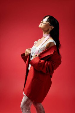 Kendine güvenen Asyalı bir kadın zarif bir şekilde ayakta duruyor, çarpıcı bir arka planın önünde modayı kucaklıyor..