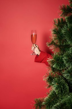 Alkolsüz bir Noel ağacının arkasından köpüklü bir içecek tutan neşeli bir el belirir..