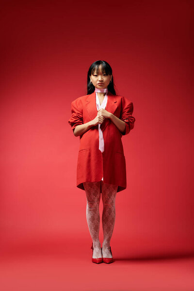 Одетые в яркий красный пиджак и трико, женщина источает элегантность и уверенность в своей позиции.