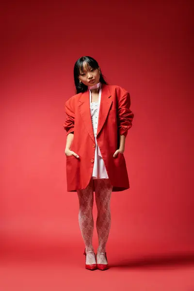 stock image A stylish young woman stands confidently, wearing a bold red coat, embodying modern fashion trends.