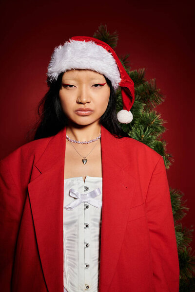 Стильная женщина уверенно позирует в шляпе Санты и элегантном наряде, принимая дух праздника.