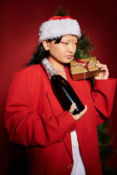 Стильная женщина в праздничном наряде держит в руках подарок и шампанское, излучая праздничное настроение.