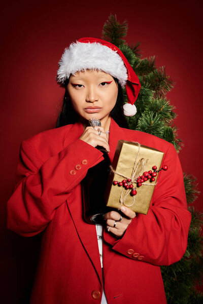 Одетый в ярко-красный костюм, женщина держит красиво обернутый подарок, источая праздничное настроение.