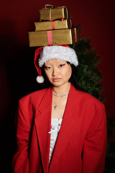 Молодая азиатка уверенно носит красный пиджак и шляпу Санты, празднуя сезон.