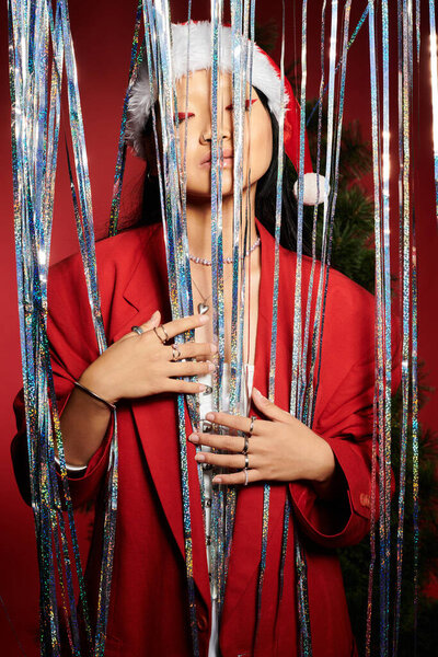 A striking woman in festive attire poses gracefully surrounded by sparkling tinsel.